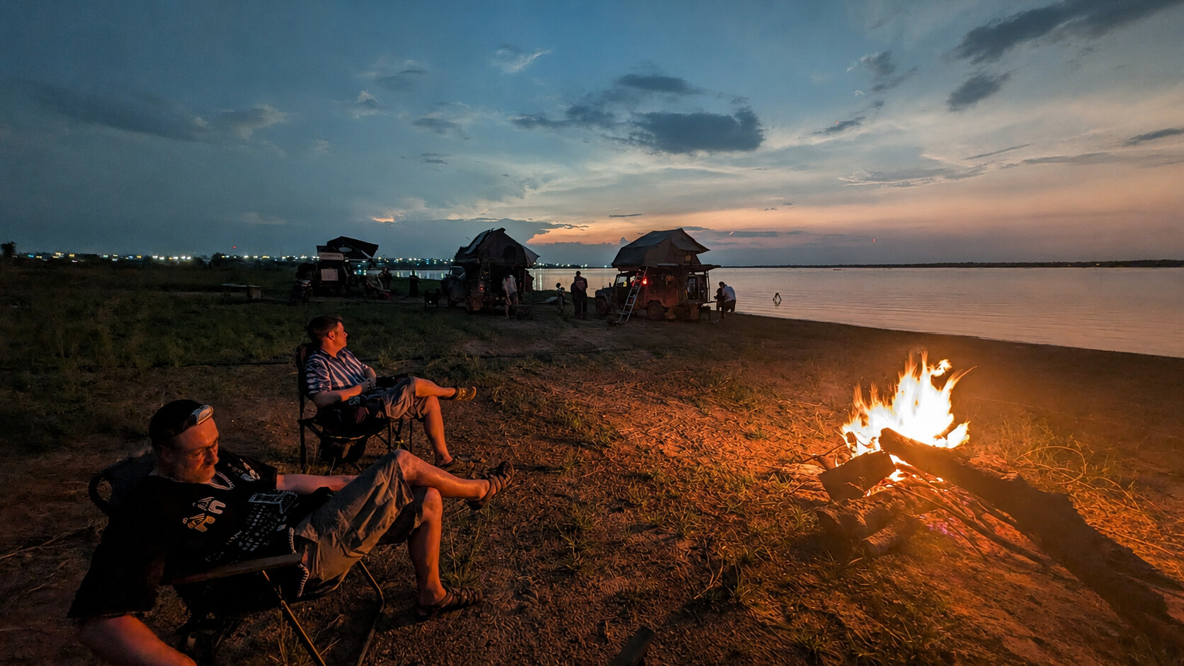 Overland travellers resting beside a campfire on the Oti River at sunset